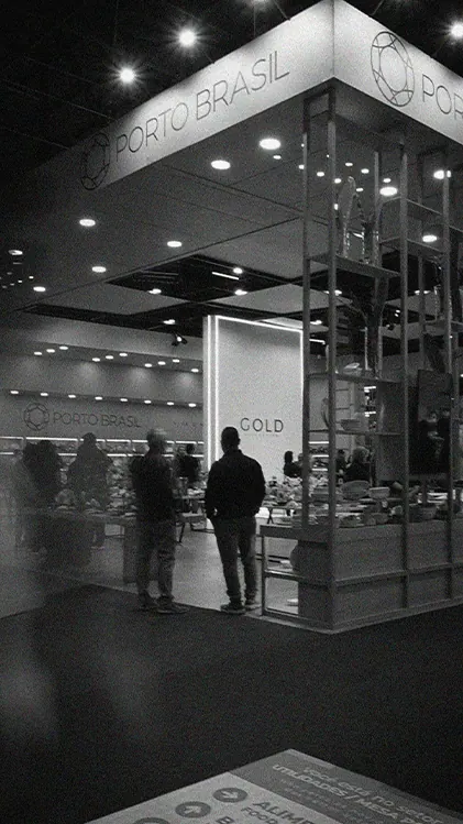 Estande da Porto Brasil numa feira, em preto e branco, com visitantes