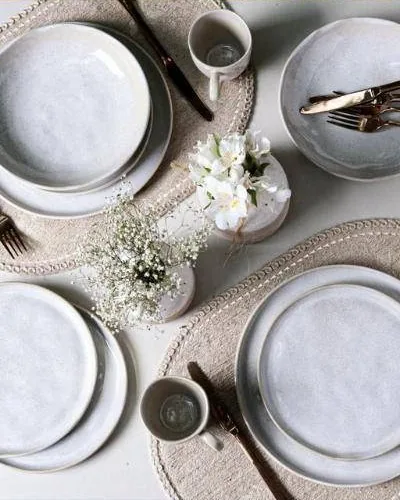 Mesa posta vista de cima, com pratos claros, flores e jogo americano